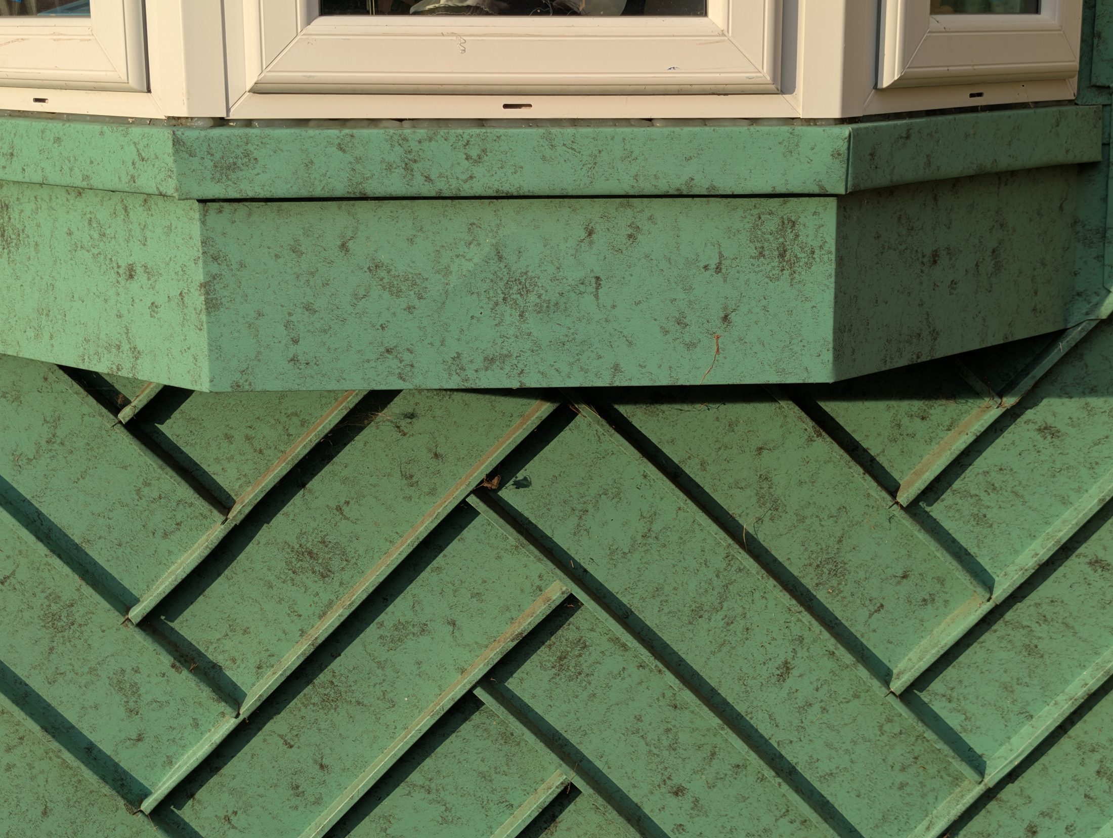 Green zinc herringbone standing-seam detail beneath a window.